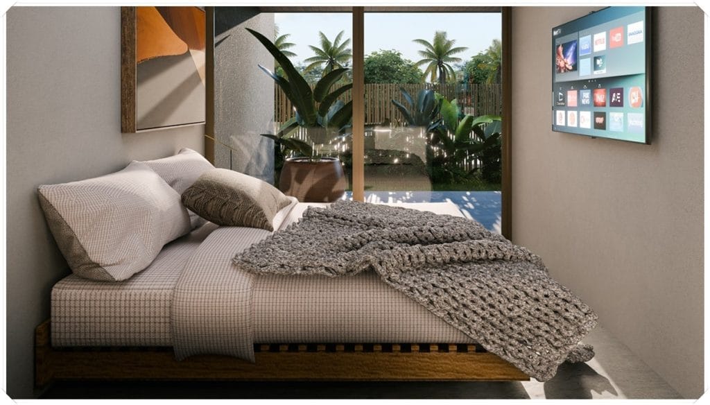 Quarto aconchegante com cama, cobertor de tricô e TV na parede, rodeado por plantas e vista para a área externa com palmeiras.