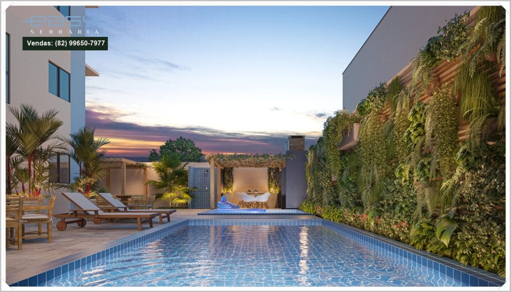 Piscina com borda de azulejos, espreguiçadeiras ao redor, cercada por vegetação e parede verde, sob um céu colorido ao entardecer.