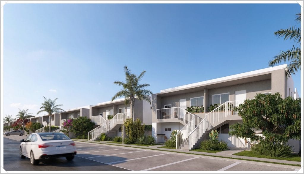 Conjunto de casas residenciais em Maceió, com plantas verdes, palmeiras e varandas, sob céu azul claro. Automóvel na rua.