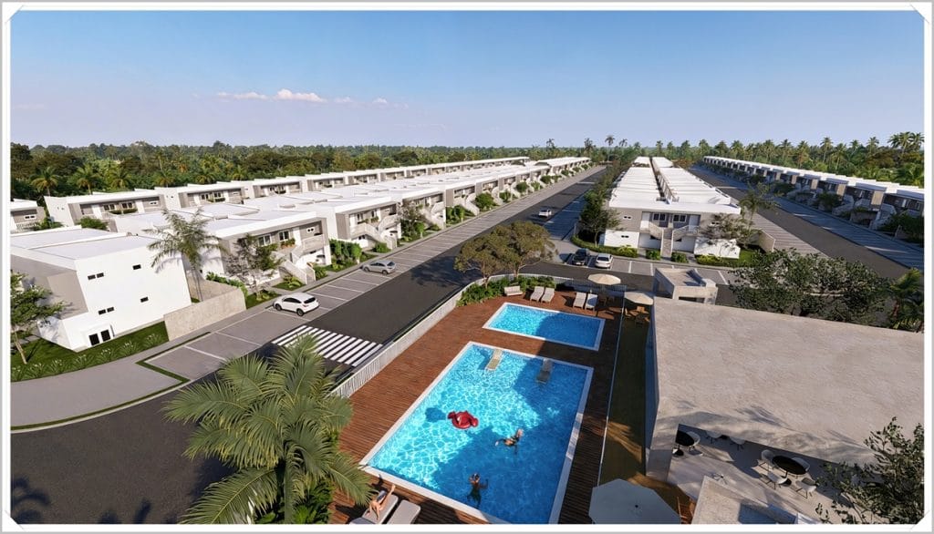 Vista aérea de um condomínio moderno com prédios brancos, área de piscina azul e vegetação ao redor, em clima tropical.